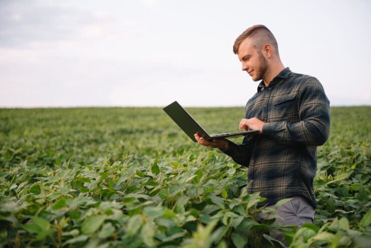 Homem no meio de uma lavoura de soja com um notebook